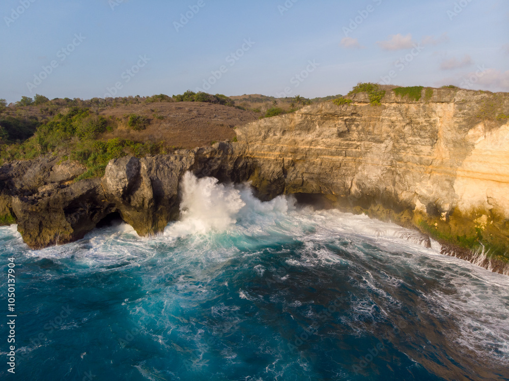 Naklejka premium Waves crashing against the rocky cliffs under a clear sky.