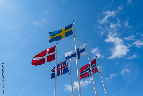 Scandinavian countries flags waving on metal poles against blue sky.