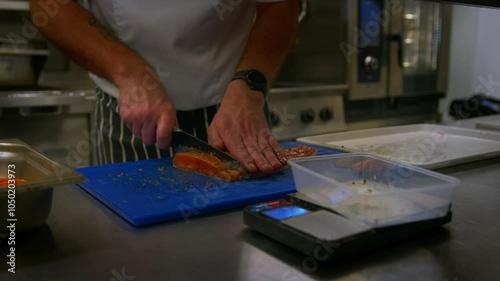 Professional chef cuts up fish as he prepares food in a professional kitchen