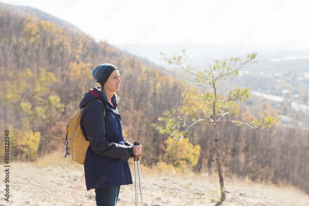 middle aged woman with a backpack and with walking sticks enjoying the autumn landscape standing on the mountain and walks in autumn outdoor. copy space. mental health. Slow life. middle aged woman with a backpack and with walking sticks enjoying the autumn landscape standing on the mountain and walks in autumn outdoor. copy space. mental health. Slow life.