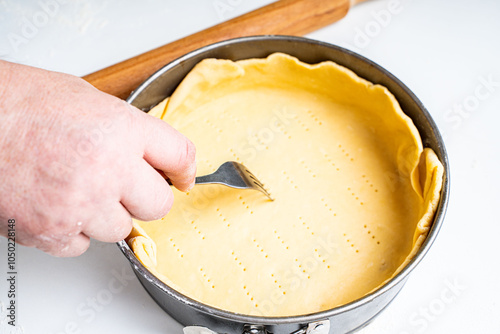 The dough, laid out in a baking dish, the hand makes punctures in the dough with a fork. Pie recipe