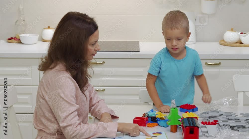 Mother and child playing together at home. Woman and little boy having fun assemble a kids plastic toy train with track set.