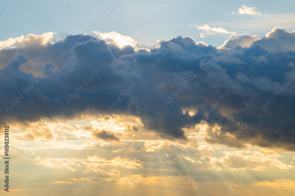 Obraz premium Dramatic clouds illuminated by sunset glow over tranquil sky creates a serene evening atmosphere in nature