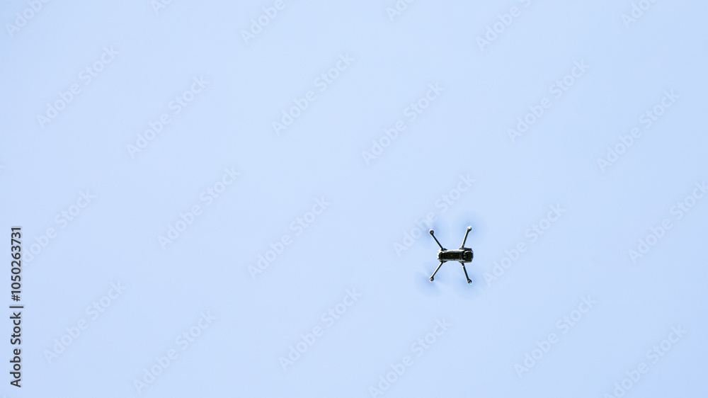 Fototapeta premium A solitary drone flies high against a clear blue sky, symbolizing technology and modern aerial surveillance challenges