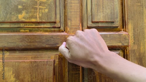 Close-up of a man knocking on a house door, with clenched fists knocking on the door slowly. House door made of wood.
