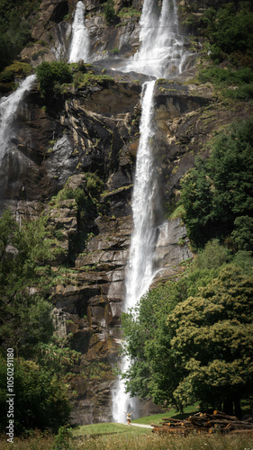 A female woman is walking towards the stunning Acquafraggia waterfall in Borgonuovo, Lombardy, Italy.