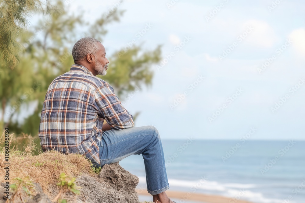An African grandfather of 65 years enjoys a moment of tranquility while looking out over the ocean horizon from a cliff. The soft dawn light creates a peaceful atmosphere, enhancing the minimalist bac An African grandfather of 65 years enjoys a moment of tranquility while looking out over the ocean horizon from a cliff. The soft dawn light creates a peaceful atmosphere, enhancing the minimalist bac