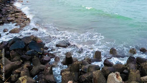 View of a concrete tetrapod installed on a beach, the concrete is made as a breakwater for sea water, preventing abrasion. Waves of sea water crashing into a concrete tetrapod.