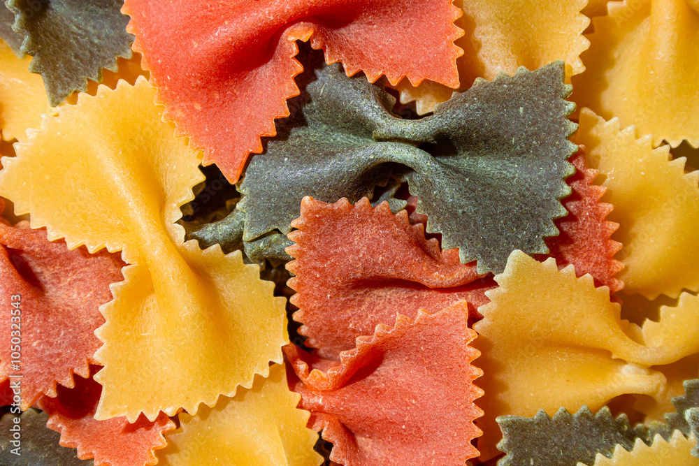 Uncooked Vibrant Colored Farfalle Pasta: A Culinary Canvas of Multicolored Bow-Tie Macaroni, Creating a Lively and Textured Background for Gourmet Cooking Enthusiasts. Colored Dry Pasta. Raw Macaroni
