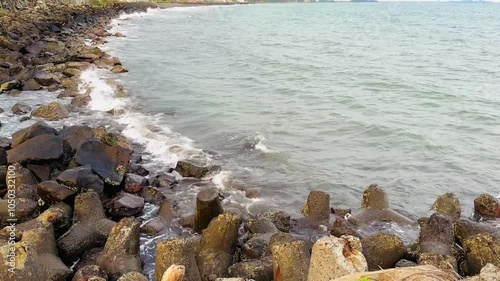 View of a concrete tetrapod installed on a beach, the concrete is made as a breakwater for sea water, preventing abrasion. Waves of sea water crashing into a concrete tetrapod.