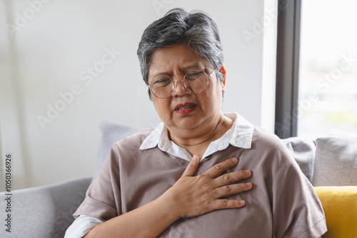 Asian elderly grabbing her chest and feeling pain from heart attack suddenly at home.