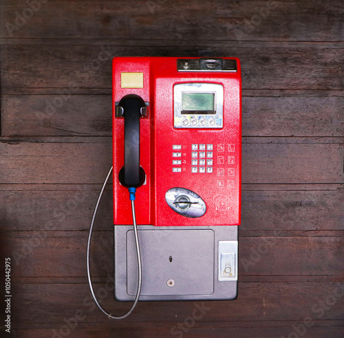 Public red old payphone coin clinging with brown wooden wall in Thailand. It is not popular now. Since most people use cell phones. But still found in the countryside. For vintage interior decoration.