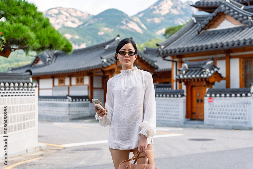 Beautiful asian female tourist wearing sunglasses with a mobile phone while looking at camera in Seoul,Travel Concept.