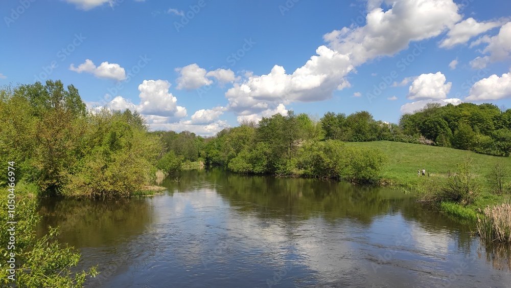 A peaceful river flowing through lush greenery under a bright blue sky with fluffy clouds during a sunny day A peaceful river flowing through lush greenery under a bright blue sky with fluffy clouds during a sunny day