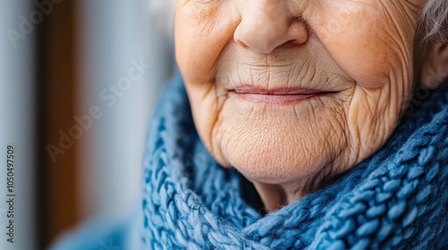 Close up of elderly woman face, showcasing her warm smile and texture of her skin, wrapped in cozy blue scarf. image conveys sense of comfort and wisdom photo