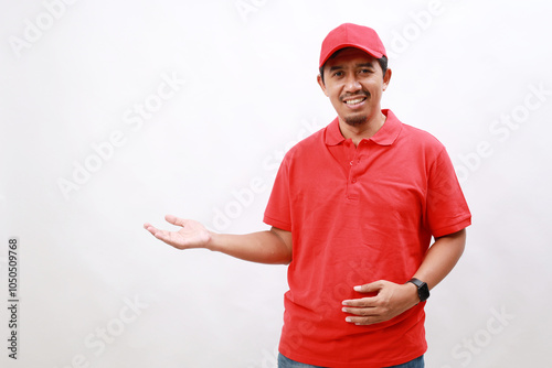 Happy delivery asian man in red uniform standing palm up hand to blank space for text advertise on isolated white background. Smiling male delivery service worker.