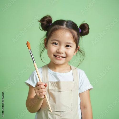 a young girl with a bright smile, holding a paintbrush in her hand against a vibrant green background.