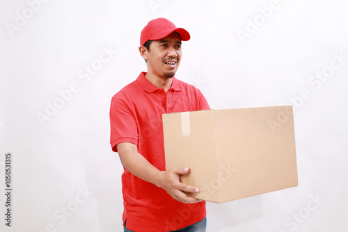 Happy asian delivery courier in red t-shirt and cap carrying and offering a box package to someone. isolated over white background