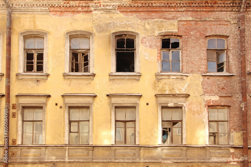 the facade of an old brick house with broken windows and crumbling plaster photo