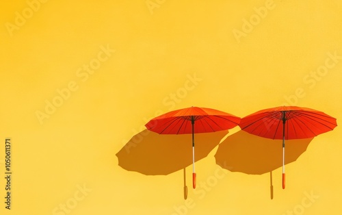 A minimalist photography composition featuring two vibrant orange umbrellas against a bright yellow background.