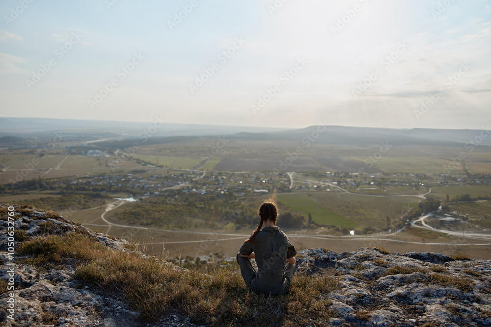 Fototapeta premium Person sitting on hill overlooking valley and town below on travel adventure trip discovery beauty nature landscape viewoptionsmenu