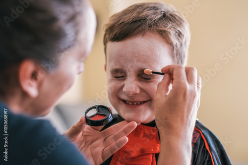 Mother applying face paint on her son for halloween costume party photo