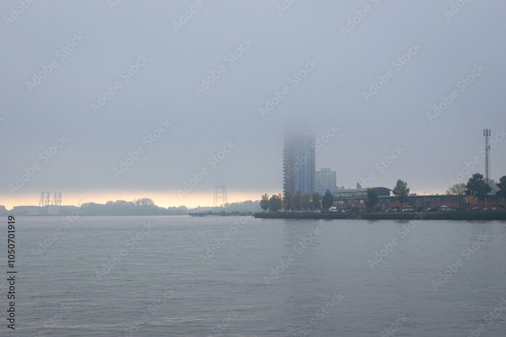 Rising fog and stratus over river Hollandsche IJssel, not far from Rotterdam, Netherlands. The tall flats are still with their tops in the clouds, while it is already clearing nicely on the horizon. Rising fog and stratus over river Hollandsche IJssel, not far from Rotterdam, Netherlands. The tall flats are still with their tops in the clouds, while it is already clearing nicely on the horizon.