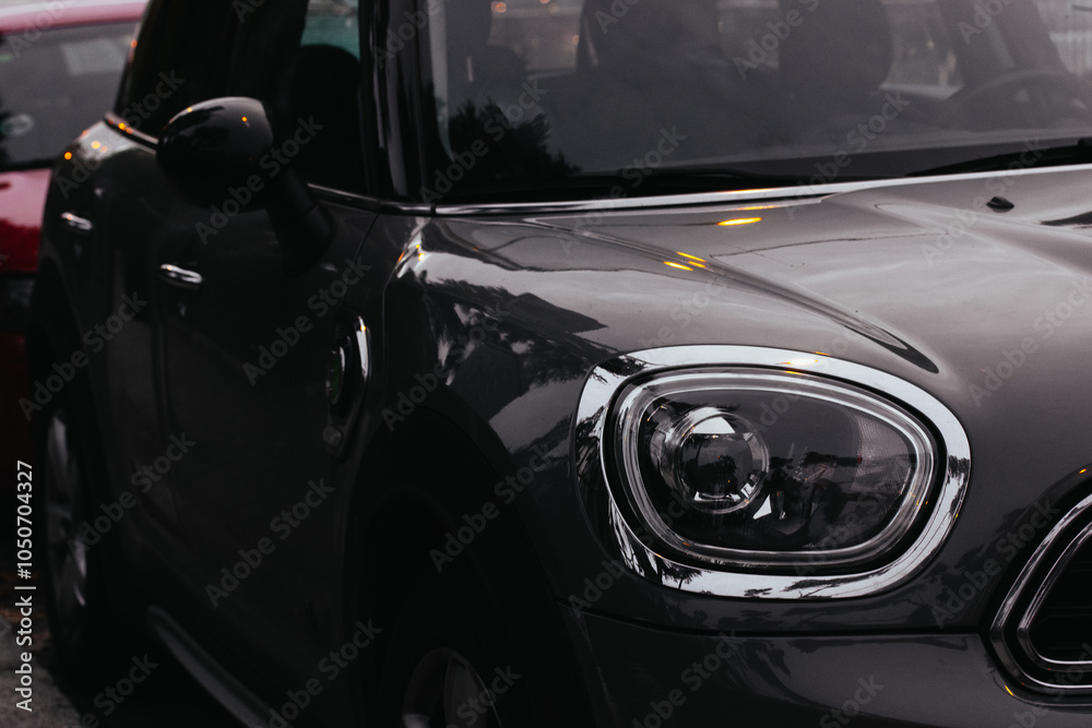 Headlight and hood of a black car with shiny exterior close-up. Stylish modern automobile in dark key. The cars parked on the evening city street. Headlight and hood of a black car with shiny exterior close-up. Stylish modern automobile in dark key. The cars parked on the evening city street.