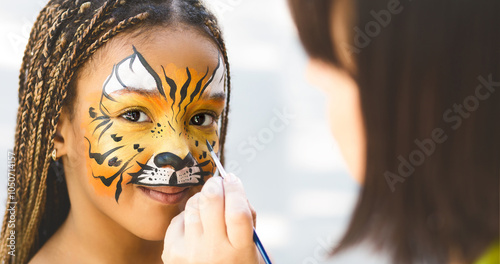 Adorable african-american girl getting tiger face painting in park, empty space photo