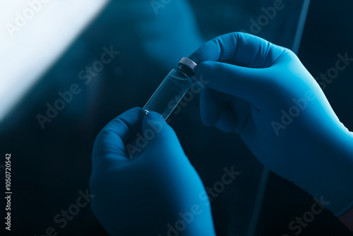 A blue-gloved medic's hand holds a vaccine or test tube