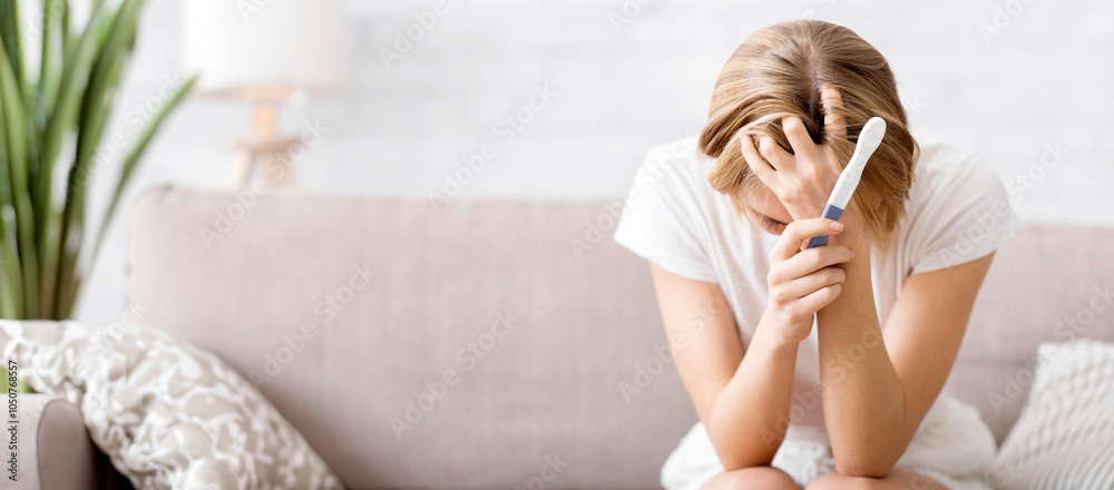 © Prostock-studio - Lost young woman with pregnancy test sitting on couch at home and holding her head, unplanned pregnancy