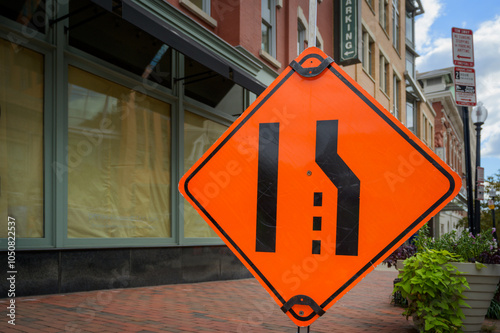 Large orange lane closed merge sign on urban sidewalk space for copy.