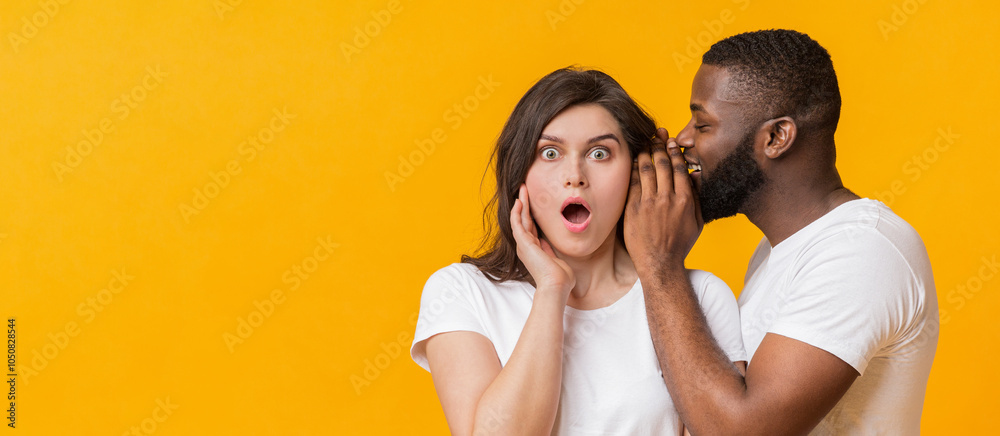 Obraz premium African American Man Sharing Secret With His Girfriend. Surprised Woman Opened Mouth In Shock, Yellow Studio Background With Free Space