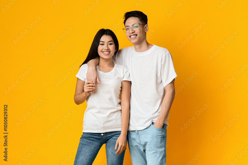 Asian guy hugging his smiling girlfriend, yellow studio background Asian guy hugging his smiling girlfriend, yellow studio background