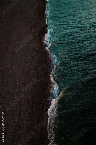 Wallpaper with a view of the dramatic meeting of dark sand and clear sea, where the waves crash on the shore.