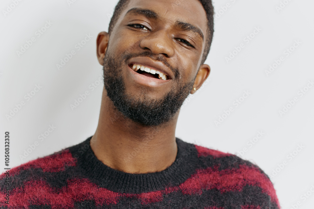Obraz premium Cheerful bearded man in red and black sweater smiling warmly, standing against a plain white background