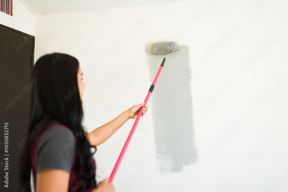 Rear view of a woman using a paint roller to paint the walls gray in her new apartment