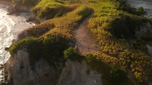 An aerial view reveals a winding dirt path through lush green hills near the coastline at Yabucoa, Puerto Rico.