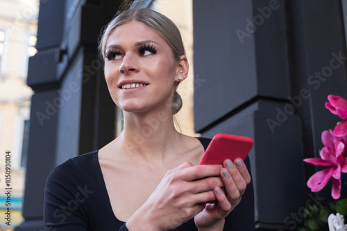 Young woman with fake eyelashes and a black shirt playing on red cellphone photo