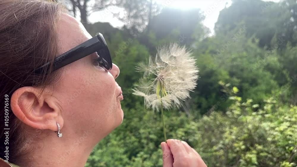 Portrait of beautiful mature woman blowing dandelion seeds