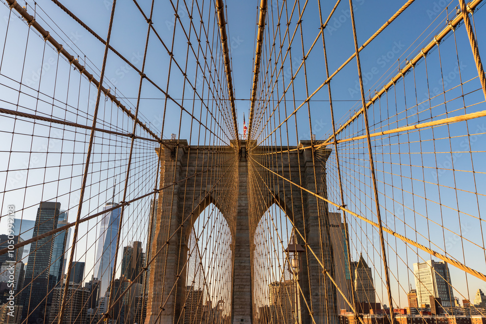 Fototapeta premium View of the Brooklyn Bridge's Gothic Granite Tower and Cables with US Flag on top and 1875 year visible