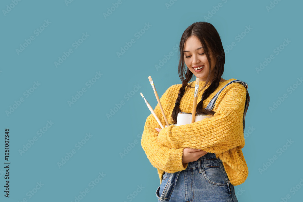 Female Asian artist with paint cans and brushes on blue background Female Asian artist with paint cans and brushes on blue background