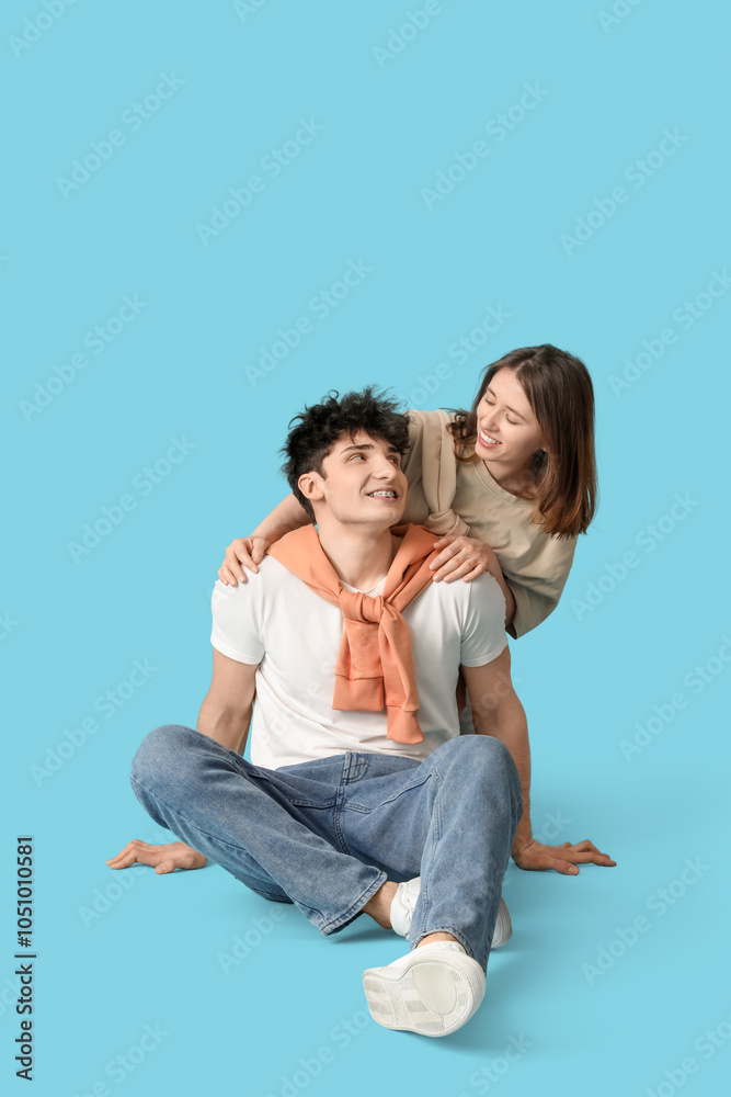 Fototapeta premium Young beautiful couple in stylish clothes sitting on floor on blue background