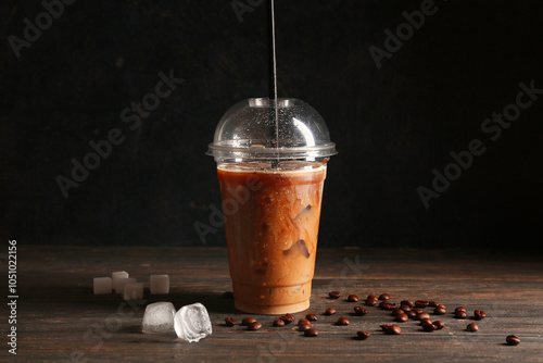 Plastic cup of iced latte and coffee beans on wooden table photo