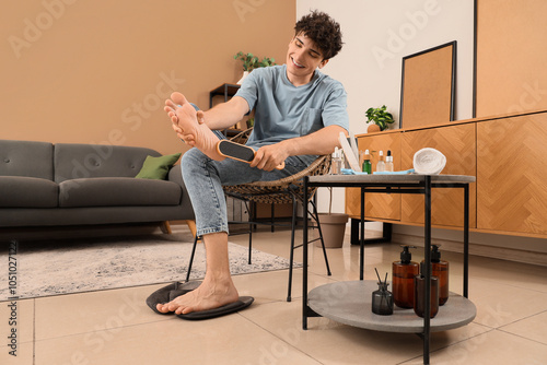 Handsome young happy man with pumice doing pedicure at home photo