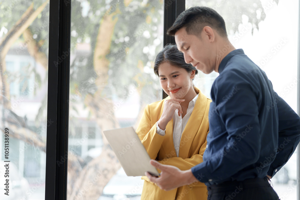 A professional woman in a yellow blazer presents a laptop to a colleague in a bright, modern office setting. A professional woman in a yellow blazer presents a laptop to a colleague in a bright, modern office setting.