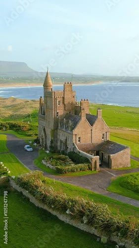 Spectacular aerial vertical orbit sunset view of Classiebawn Castle and Mullaghmore Head with huge waves rolling ashore. Speed ramp effect. Signature point of the Wild Atlantic Way, Co. Sligo, Ireland