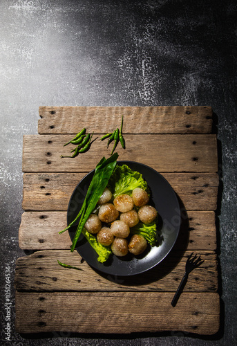 Pork-filled sago in a black plate with long leaf coriander and lettuce on an old wooden table with green chilli peppers on a wooden table