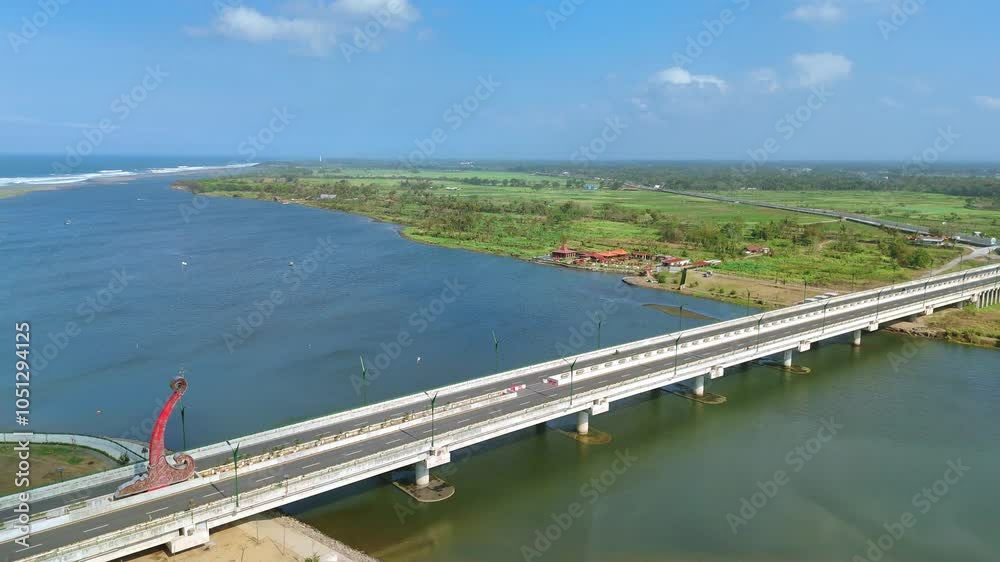 Aerial view of a bridge spanning a river estuary with view of wavy coastline. Blue sky on the horizon. Kretek II Bridge, Depok Beach, Indonesia. Aerial view of a bridge spanning a river estuary with view of wavy coastline. Blue sky on the horizon. Kretek II Bridge, Depok Beach, Indonesia.