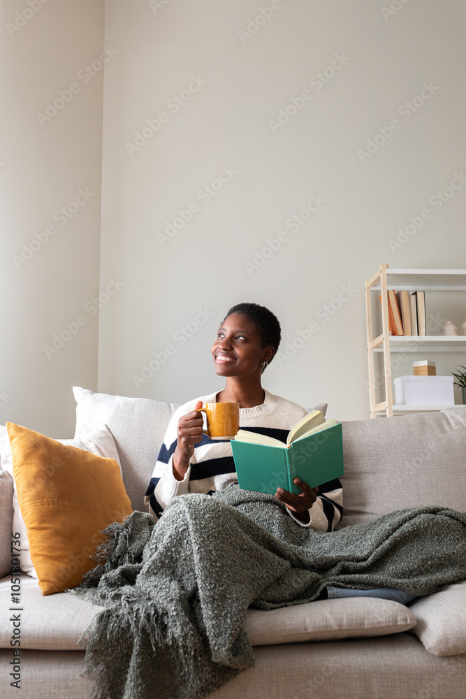 Vertical portrait of pensive relaxed African american woman reading a book at home, drinking coffee sitting on couch. Vertical portrait of pensive relaxed African american woman reading a book at home, drinking coffee sitting on couch.